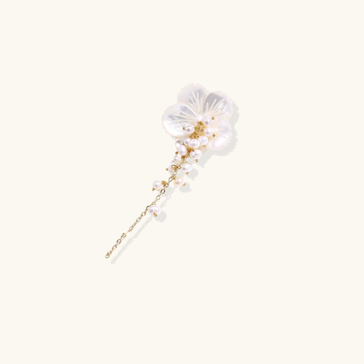 Iridescent shell flower brooch with carved petals and cascading freshwater pearls on gold chain against cream background.