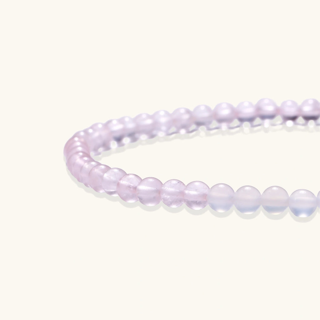 Double-wrap lavender beaded bracelet with rose quartz, pearls, gold vermeil charm and pink tassel on white background.