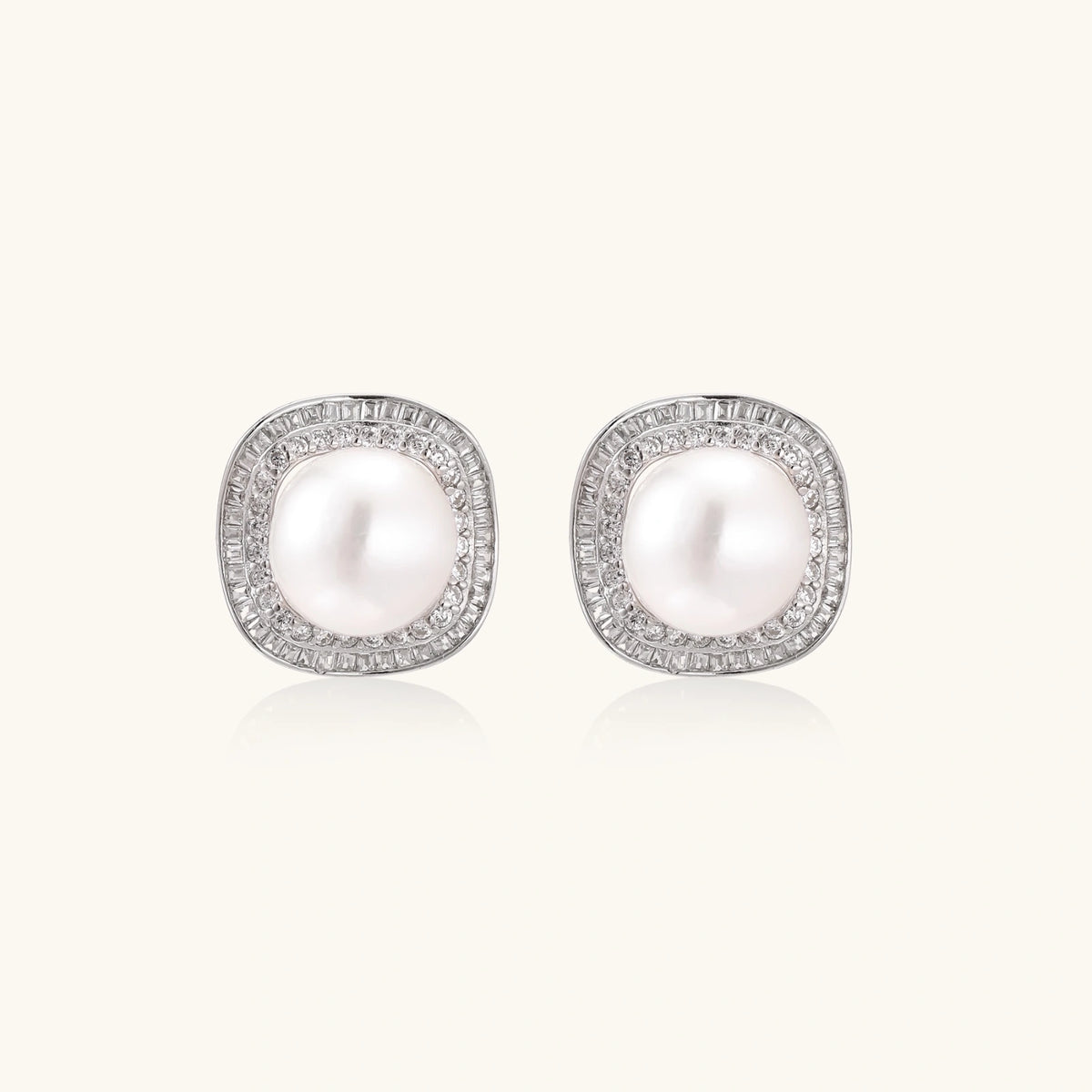 Rhodium-plated sterling silver stud earrings with round freshwater pearls surrounded by geometric crystal halos on cream background.