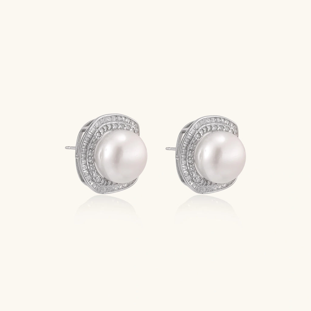 Rhodium-plated sterling silver stud earrings with round freshwater pearls surrounded by geometric crystal halos on cream background.