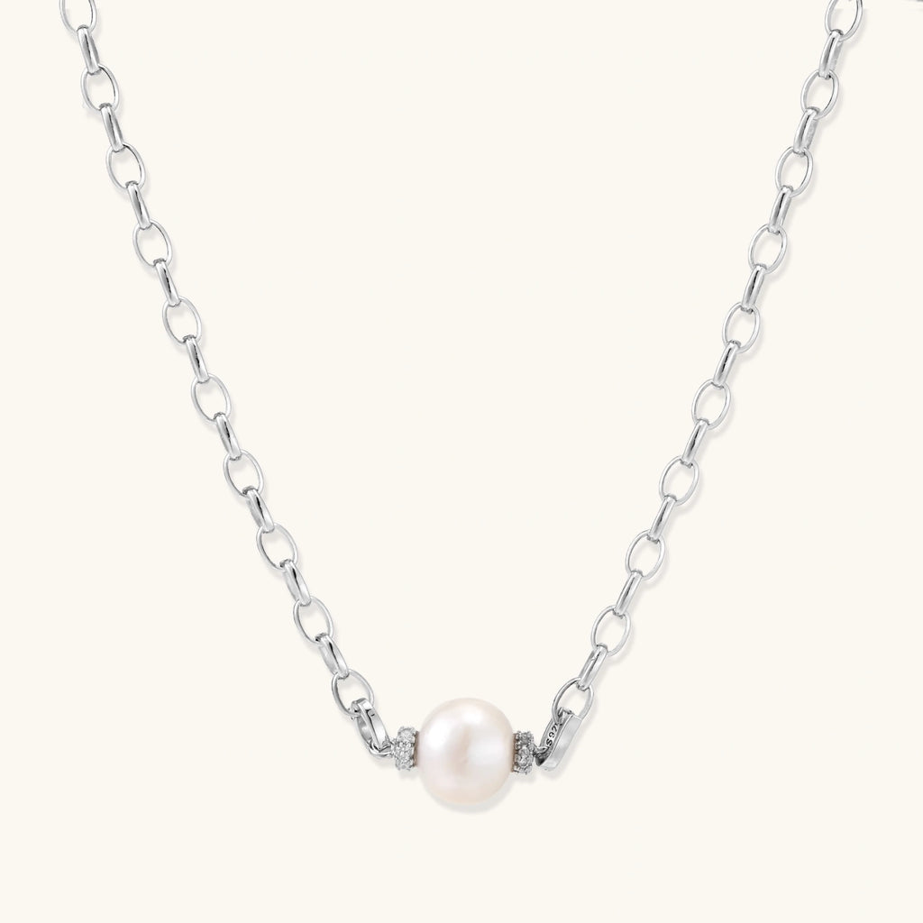 Dainty rhodium-plated silver chain necklace with centered 10mm freshwater pearl and crystal accents on cream background