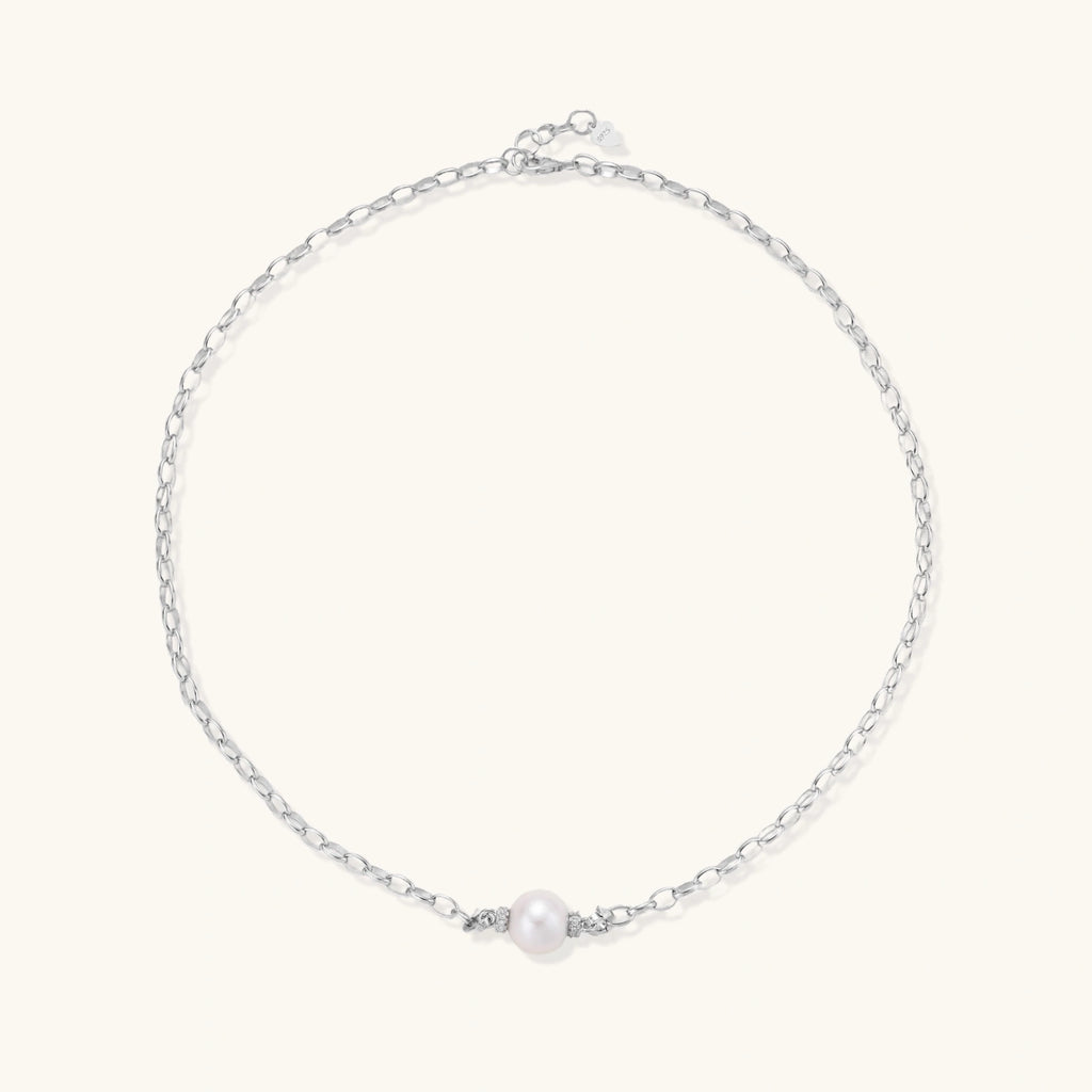 Dainty rhodium-plated silver chain necklace with centered 10mm freshwater pearl and crystal accents on cream background